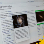 Photo of a laptop displaying the Wikipedia article about the Andromeda Galaxy, with the Wikipedia 25 Puzzle motif overlaid on top.